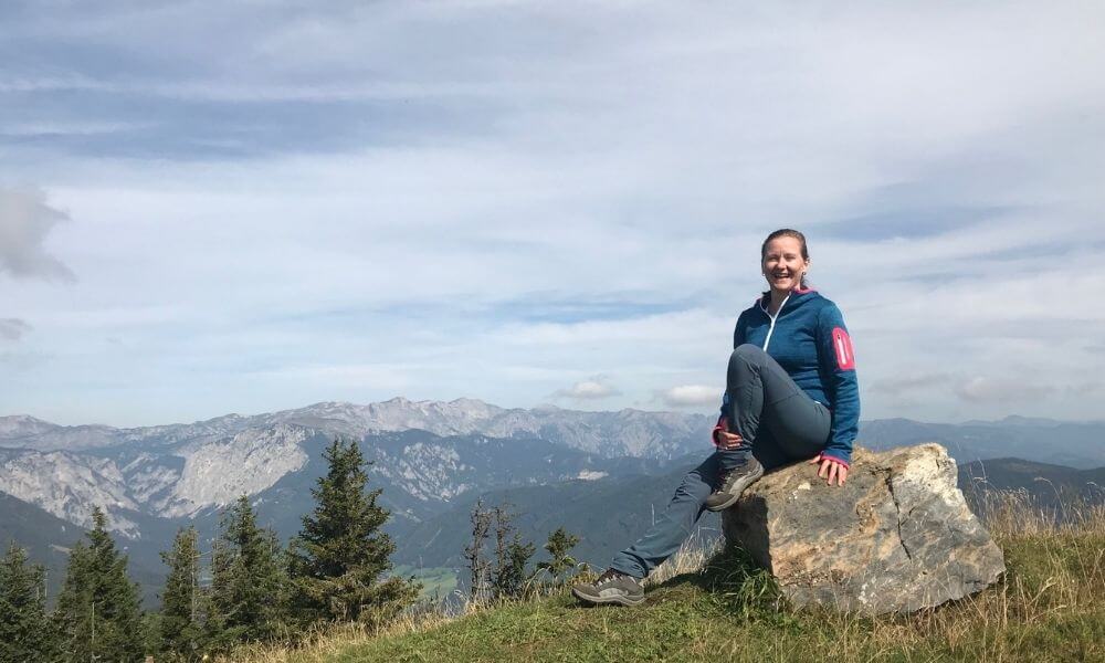 Frau sitzt auf einem Stein am Berg mit Ausblick